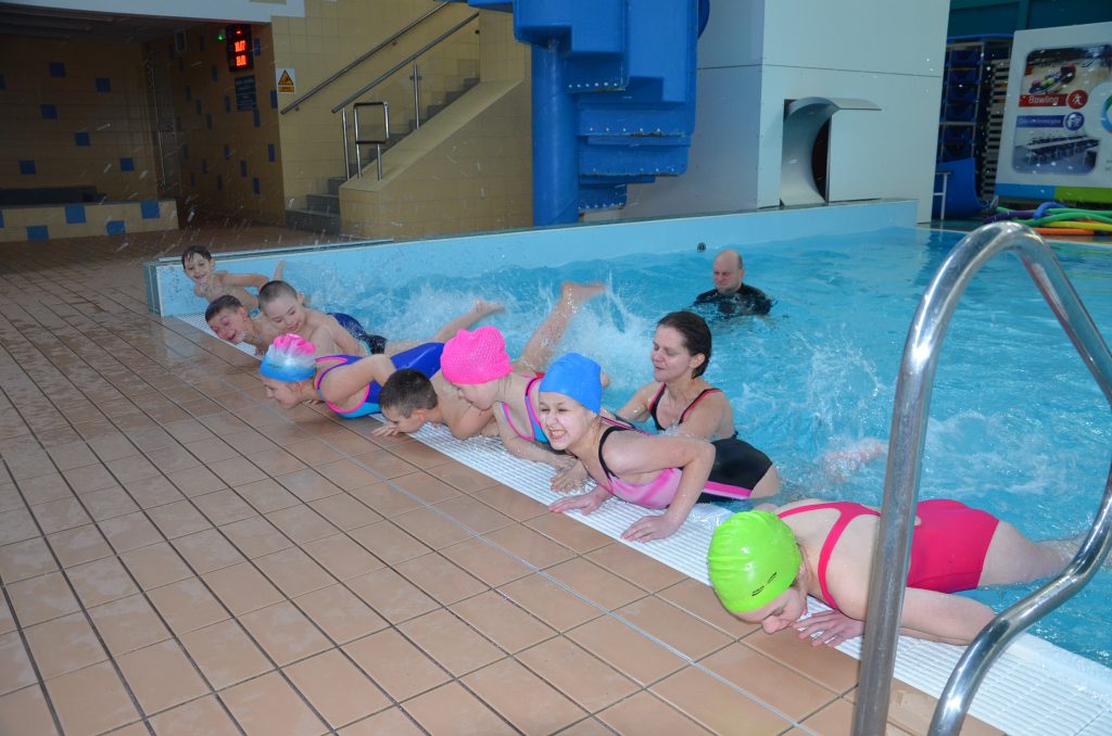 Grupa dzieci uczestniczących w zajęciach na basenie z opiekunami